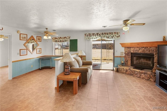 living room with visible vents, ceiling fan, a textured ceiling, a stone fireplace, and light tile patterned flooring