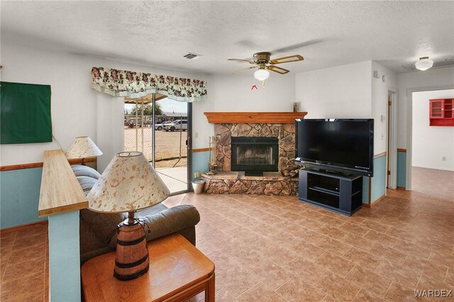 living area with a textured ceiling, a ceiling fan, and a stone fireplace