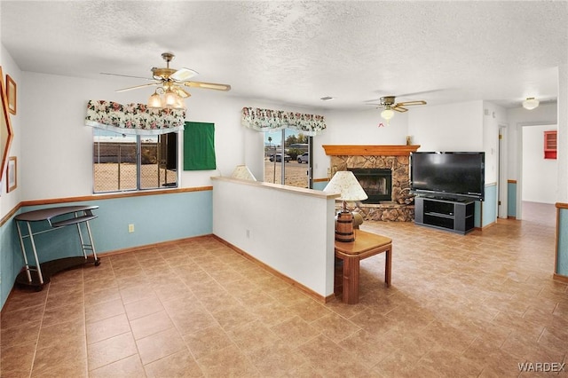 living area featuring ceiling fan, a stone fireplace, and a textured ceiling