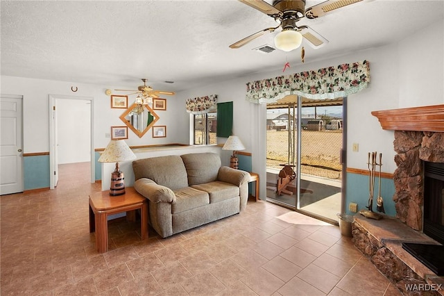 living area with a ceiling fan, visible vents, a stone fireplace, and a textured ceiling