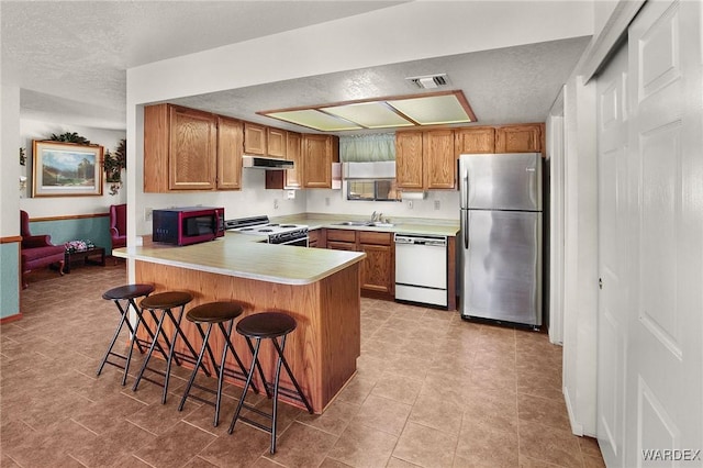 kitchen with visible vents, light countertops, white appliances, a peninsula, and a kitchen bar