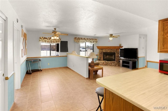 kitchen featuring light tile patterned floors, open floor plan, ceiling fan, a stone fireplace, and a textured ceiling