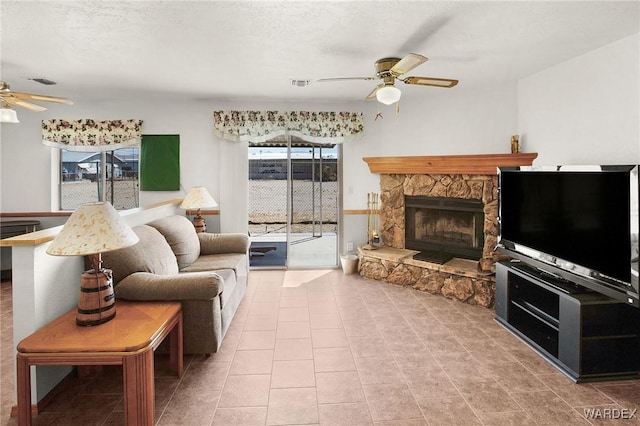 tiled living room with visible vents, ceiling fan, and a stone fireplace