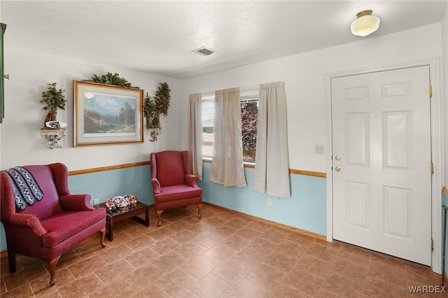 sitting room with baseboards, visible vents, and a textured ceiling