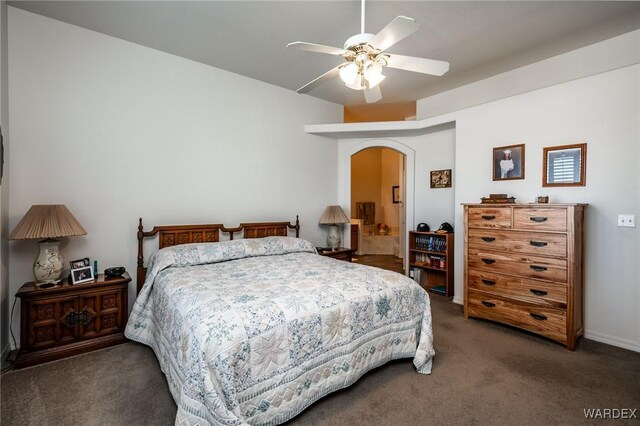 bedroom featuring arched walkways, dark colored carpet, a ceiling fan, and ensuite bathroom