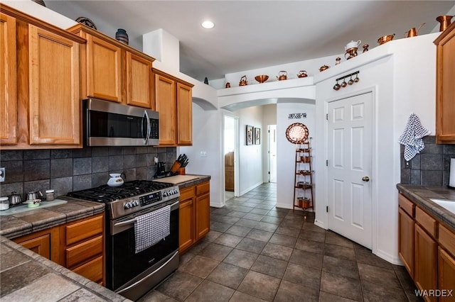 kitchen featuring tile countertops, appliances with stainless steel finishes, arched walkways, and backsplash