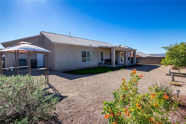 back of property with cooling unit, a fenced backyard, a tile roof, a gazebo, and stucco siding