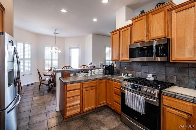 kitchen featuring a peninsula, appliances with stainless steel finishes, backsplash, brown cabinets, and decorative light fixtures