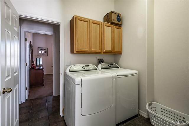 clothes washing area featuring dark tile patterned flooring, washer and clothes dryer, cabinet space, and baseboards