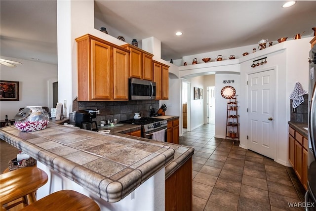 kitchen with tile countertops, a peninsula, arched walkways, and stainless steel appliances