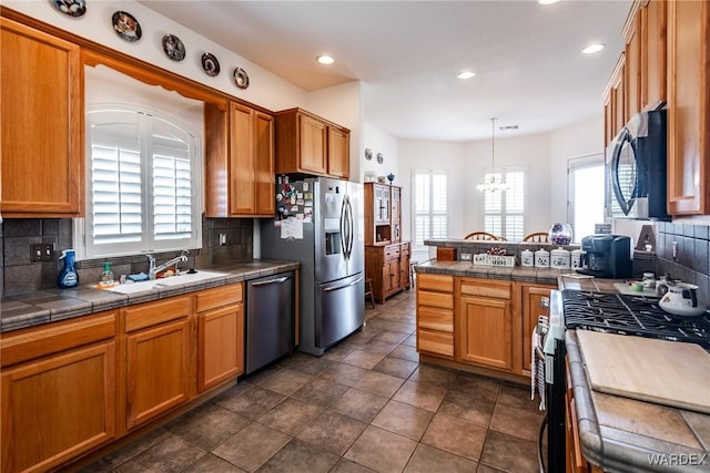 kitchen featuring a sink, hanging light fixtures, appliances with stainless steel finishes, tile counters, and tasteful backsplash