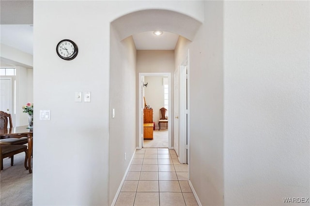 corridor with arched walkways, light tile patterned floors, and baseboards