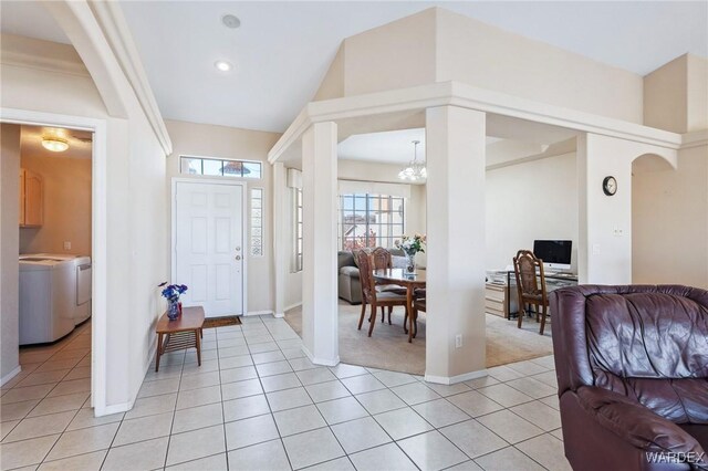 entryway with light tile patterned floors, baseboards, arched walkways, washer and dryer, and a chandelier