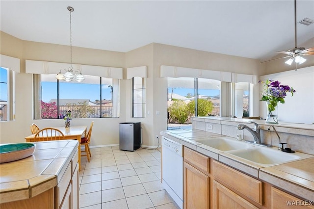 kitchen with light tile patterned floors, white dishwasher, ceiling fan with notable chandelier, a sink, and tile counters