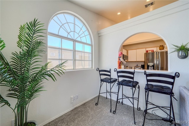 carpeted dining room with arched walkways, visible vents, and baseboards