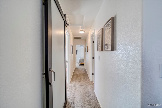 hall featuring light carpet, visible vents, and a textured wall