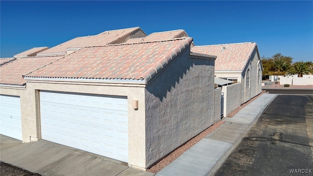 view of home's exterior with a garage, a tiled roof, and stucco siding