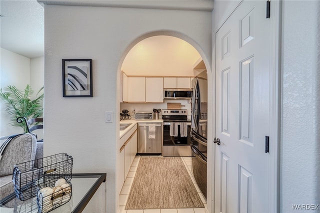 kitchen with arched walkways, stainless steel appliances, light countertops, and light tile patterned flooring