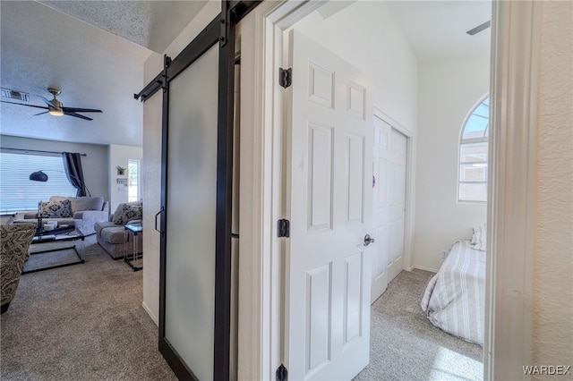 hallway with carpet floors, visible vents, a textured ceiling, and a barn door