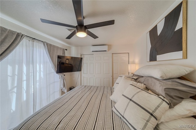 bedroom featuring a textured ceiling, an AC wall unit, a closet, and a ceiling fan