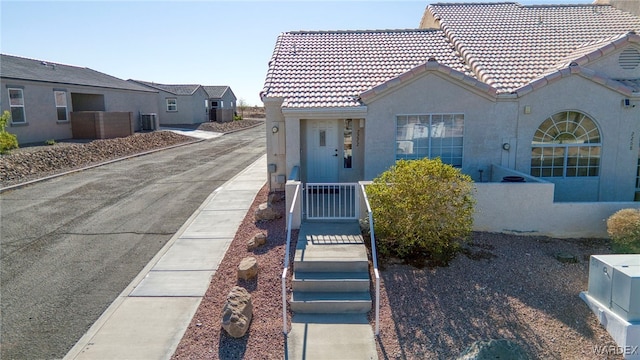 view of front facade with central AC unit, a tiled roof, fence, and stucco siding