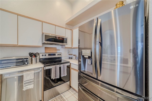 kitchen featuring a toaster, light tile patterned floors, stainless steel appliances, light countertops, and white cabinets