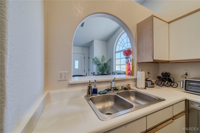 kitchen with a textured wall, arched walkways, light countertops, and a sink