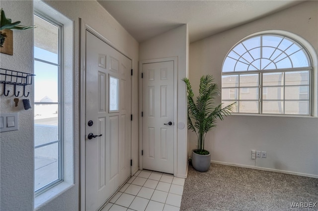 foyer entrance featuring light carpet, light tile patterned floors, and baseboards