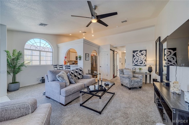 carpeted living area featuring a barn door, visible vents, a ceiling fan, vaulted ceiling, and a textured ceiling