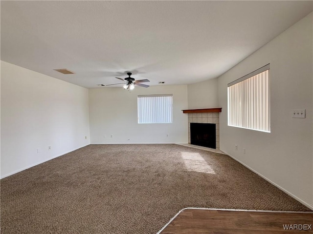 unfurnished living room with a wealth of natural light, visible vents, dark colored carpet, and a tiled fireplace