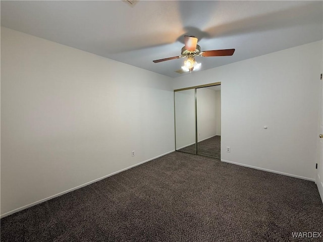 unfurnished bedroom with ceiling fan, dark colored carpet, a closet, and baseboards