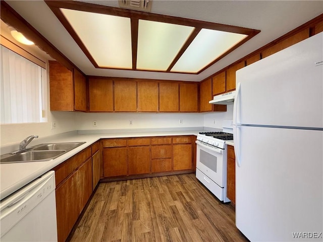 kitchen with brown cabinets, a sink, wood finished floors, white appliances, and under cabinet range hood