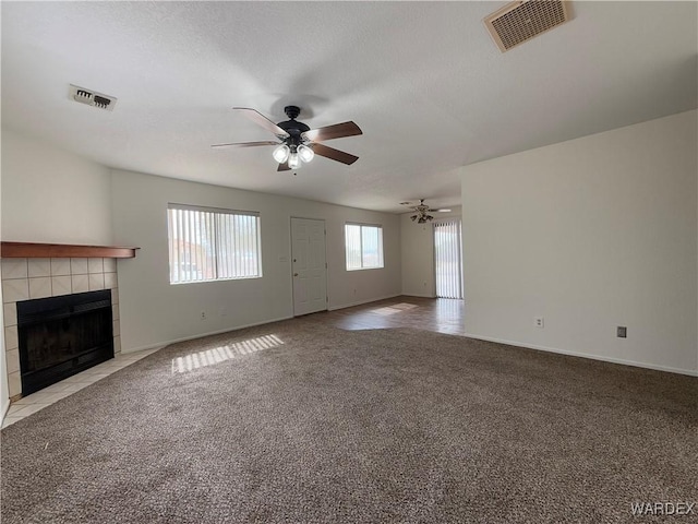 unfurnished living room featuring ceiling fan, a tile fireplace, carpet flooring, and visible vents