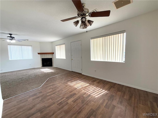 unfurnished living room featuring baseboards, visible vents, a tile fireplace, ceiling fan, and wood finished floors