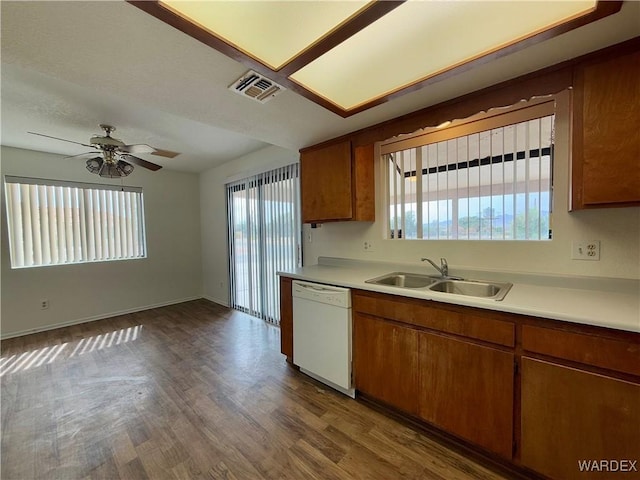 kitchen with light countertops, visible vents, brown cabinetry, white dishwasher, and a sink