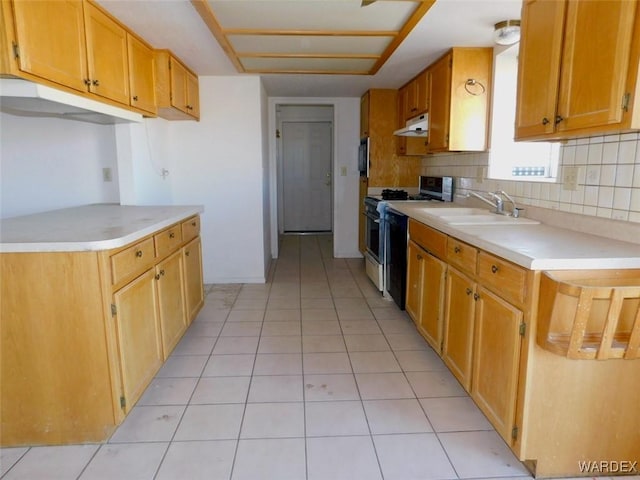 kitchen featuring light countertops, a sink, under cabinet range hood, and gas range