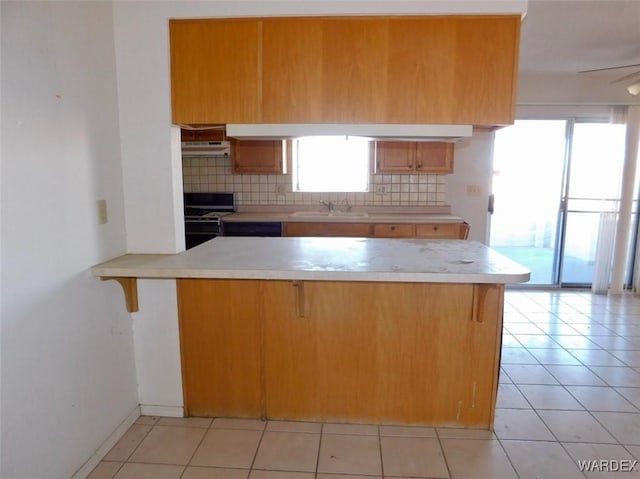 kitchen with range, a peninsula, light countertops, under cabinet range hood, and a sink