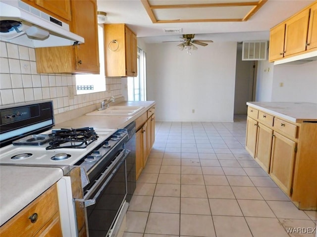 kitchen with white gas stove, under cabinet range hood, a sink, light countertops, and tasteful backsplash