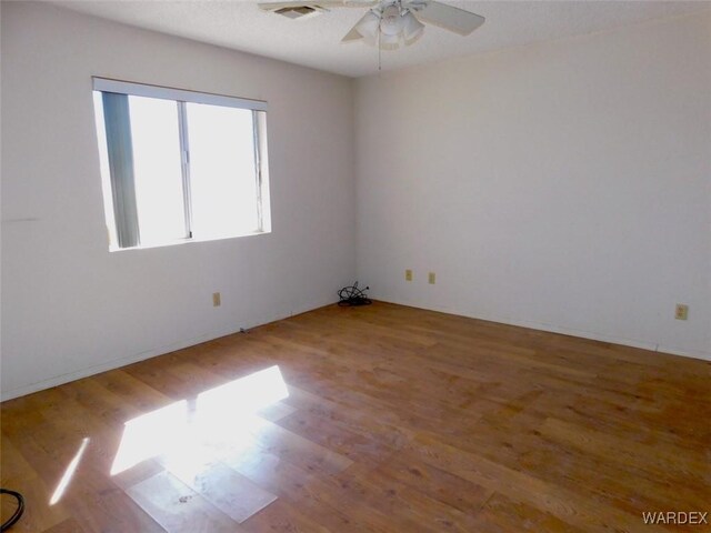 empty room featuring visible vents, ceiling fan, and wood finished floors