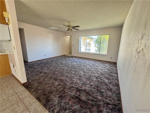 carpeted empty room with baseboards, tile patterned flooring, a textured ceiling, and a ceiling fan