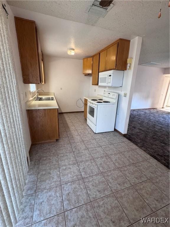 kitchen featuring white appliances, light countertops, a textured ceiling, visible vents, and a sink