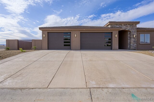 prairie-style home featuring an attached garage, fence, driveway, stone siding, and stucco siding