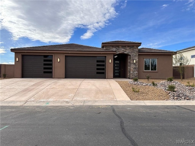 prairie-style house featuring driveway, stone siding, an attached garage, and stucco siding