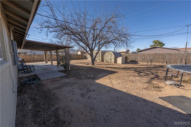 view of yard with a trampoline, an outbuilding, a patio, a storage unit, and a fenced backyard