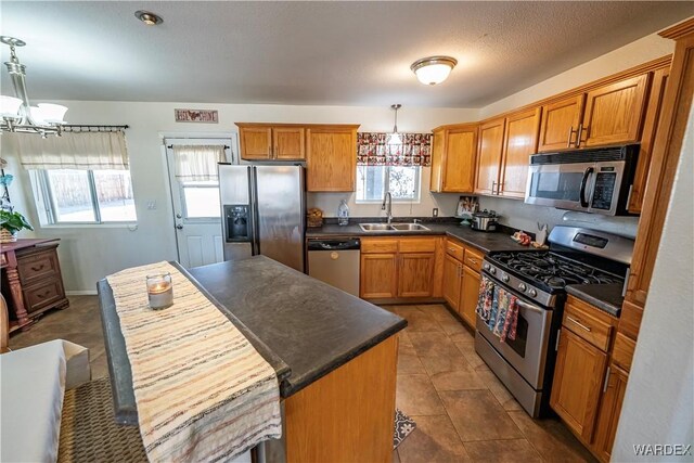 kitchen featuring dark countertops, a kitchen island, appliances with stainless steel finishes, a sink, and a notable chandelier