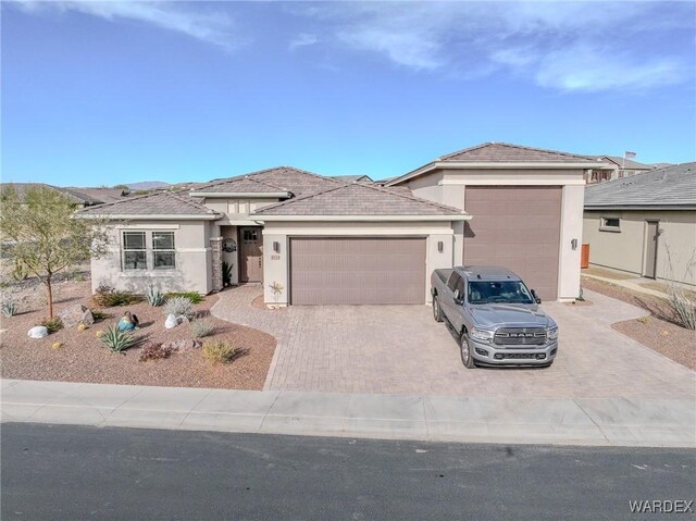 prairie-style home with decorative driveway, an attached garage, and stucco siding