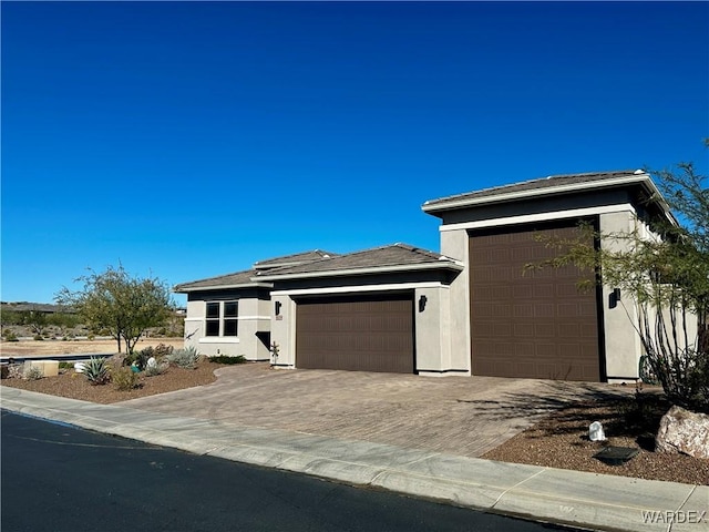 prairie-style house featuring an attached garage, decorative driveway, and stucco siding