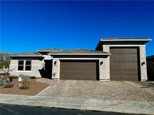 prairie-style house with a garage, decorative driveway, and stucco siding