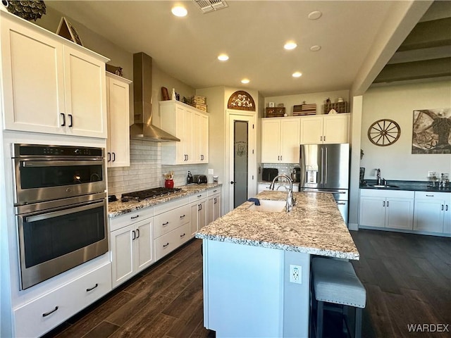 kitchen with dark wood finished floors, decorative backsplash, stainless steel appliances, wall chimney range hood, and a sink