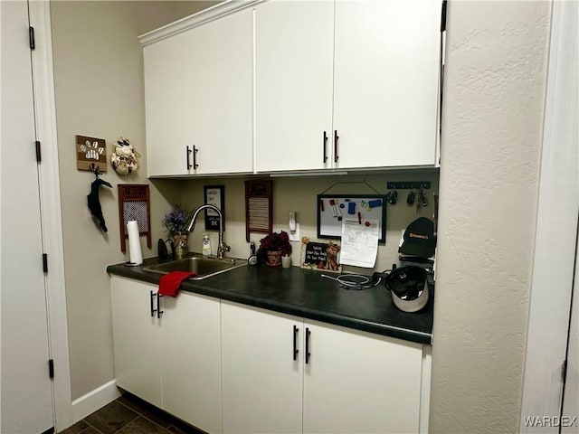 kitchen featuring dark countertops, a sink, white cabinetry, and baseboards